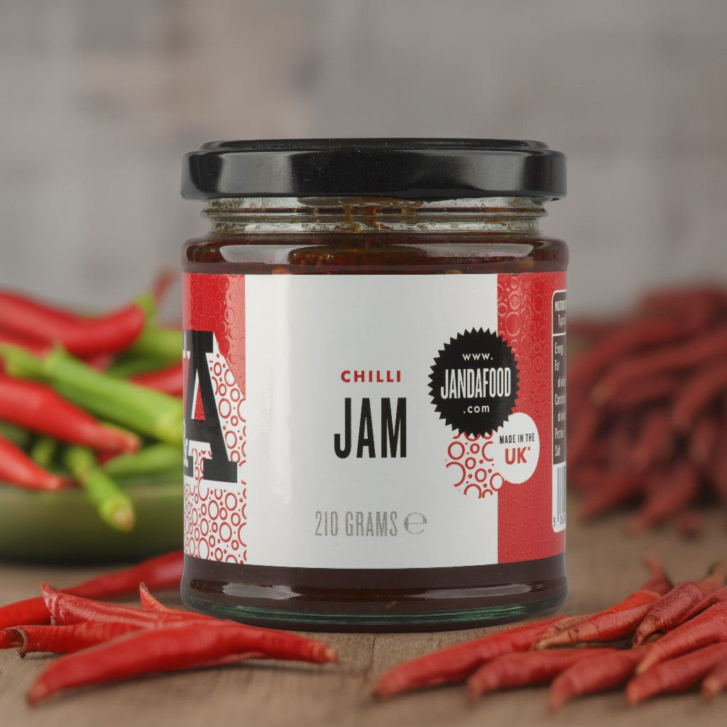 Jar of Janda Chilli Jam with red and green chilies in the background