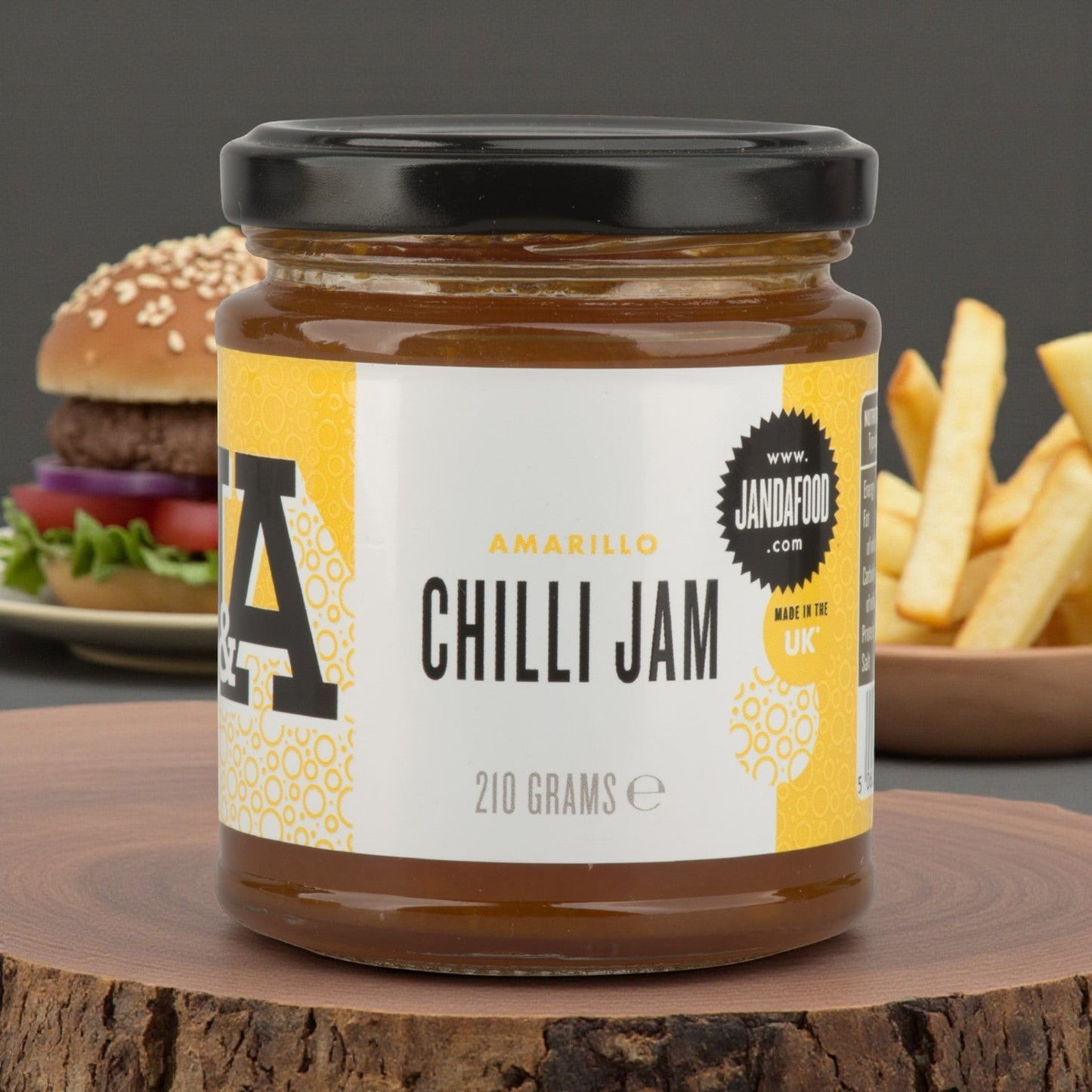 Janda Food Amarillo Yellow Chilli Jam in a glass jar on a wooden board with a burger and fries in the background