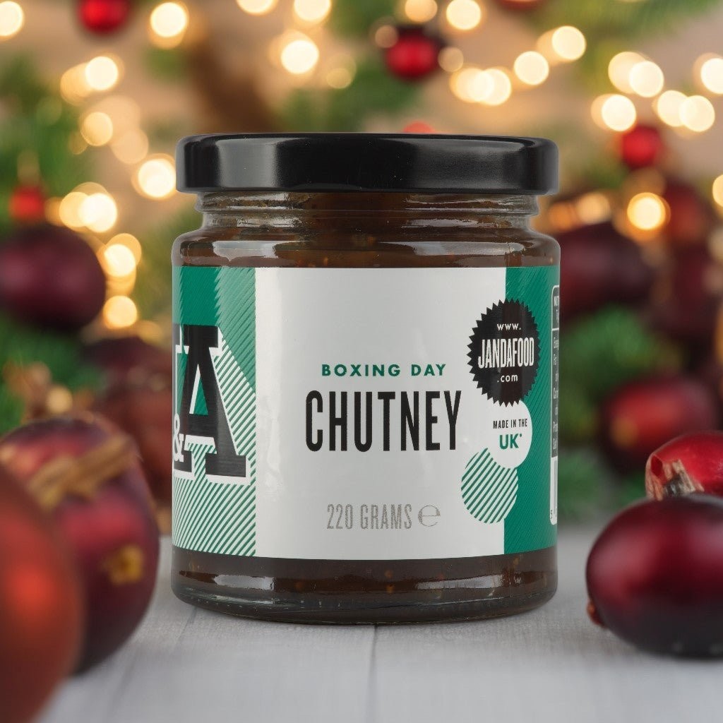 Janda Food Boxing Day Chutney in a glass jar with festive holiday decorations and bokeh lights in the background