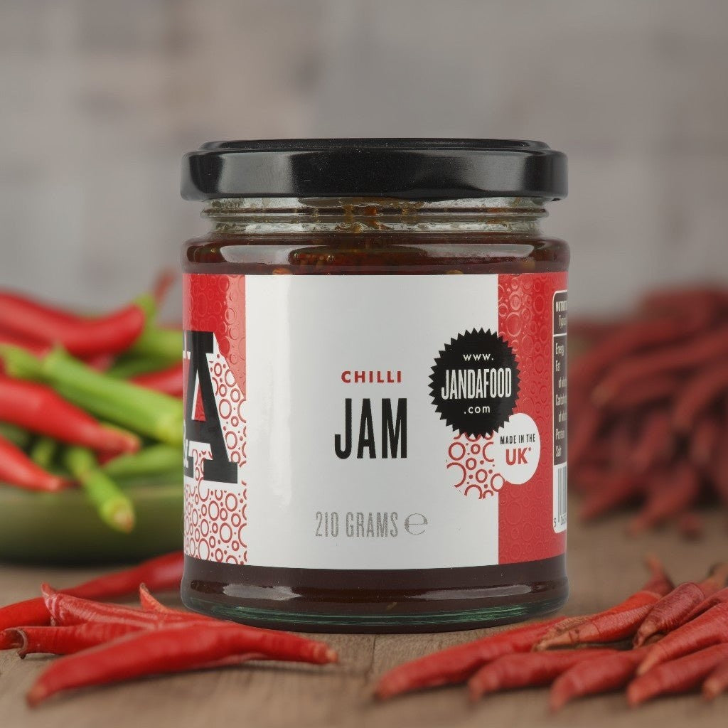 Janda Food handcrafted chilli jam in a glass jar surrounded by fresh red jalapeno chillies on a wooden surface