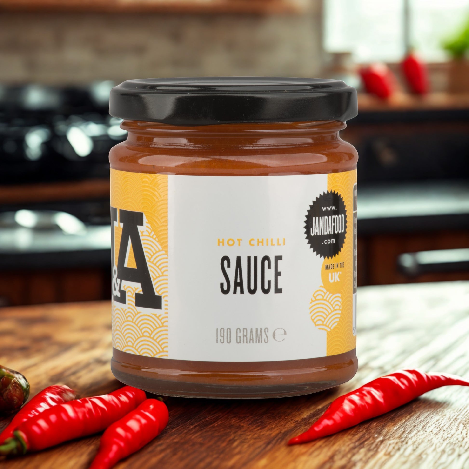 Janda Food hot chilli sauce in a glass jar with red jalapeno and habanero chillies on a wooden kitchen table