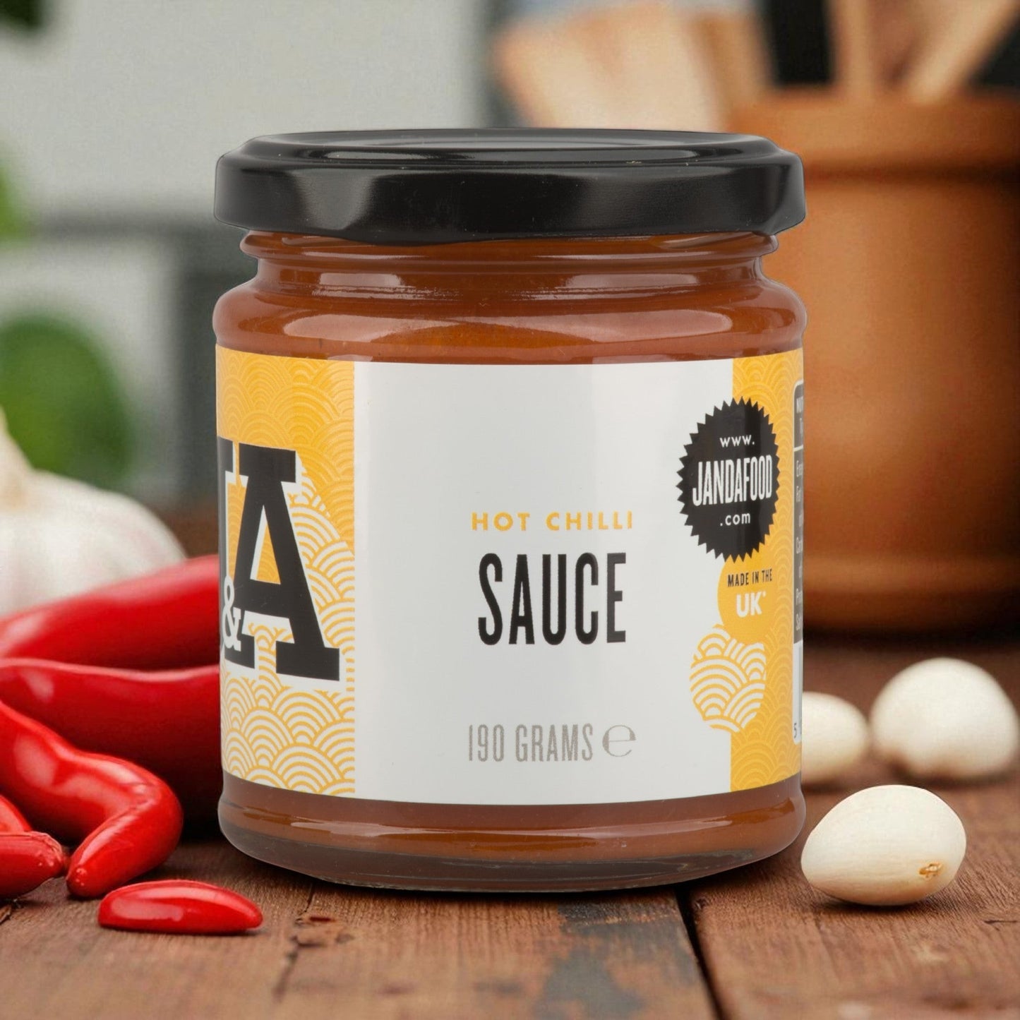 Janda Food hot chilli sauce in a 190g glass jar with red jalapeno and habanero chillies on a wooden table