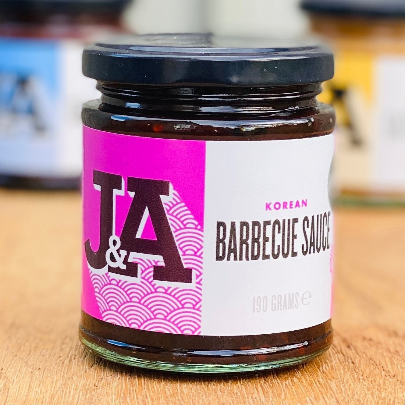 Janda Food Korean Barbecue Sauce in a glass jar with a vibrant pink and white label on a wooden surface