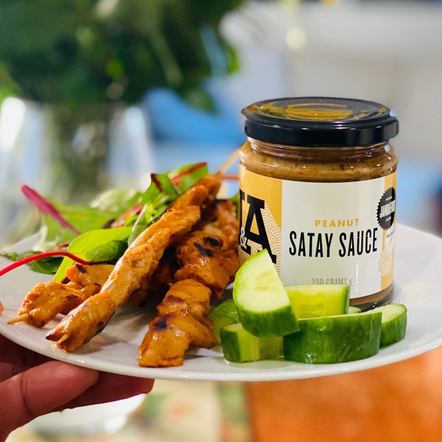 Janda Food Peanut Satay Sauce jar served with grilled chicken skewers, fresh cucumber slices, and salad greens.