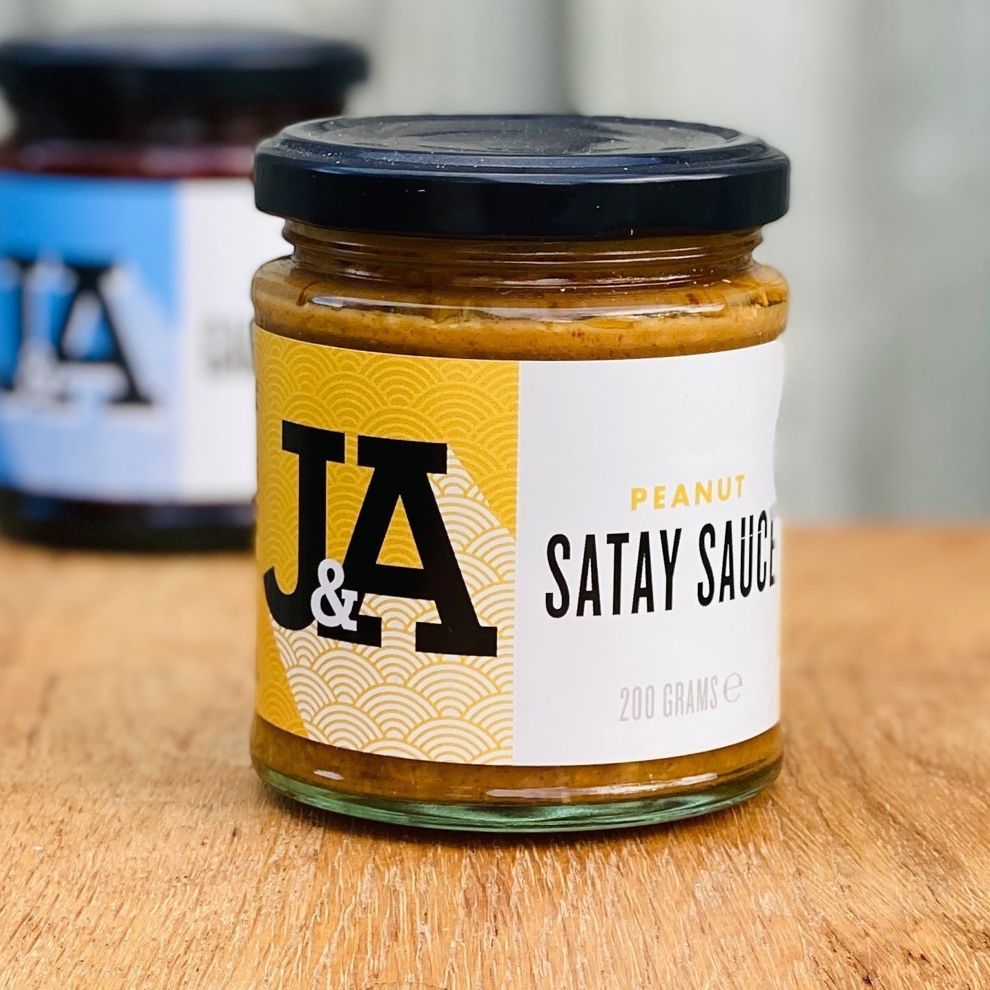 Janda Food peanut satay sauce in a glass jar with a yellow and white label on a wooden surface