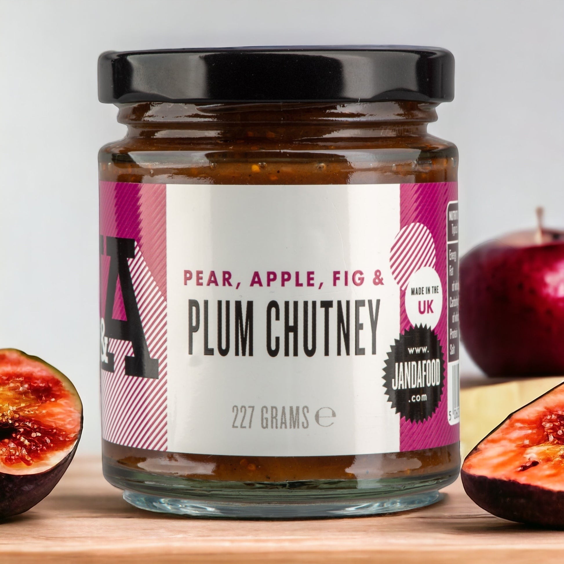 Janda Food Pear, Apple, Fig & Plum Chutney in a glass jar, surrounded by fresh sliced figs and a red apple.