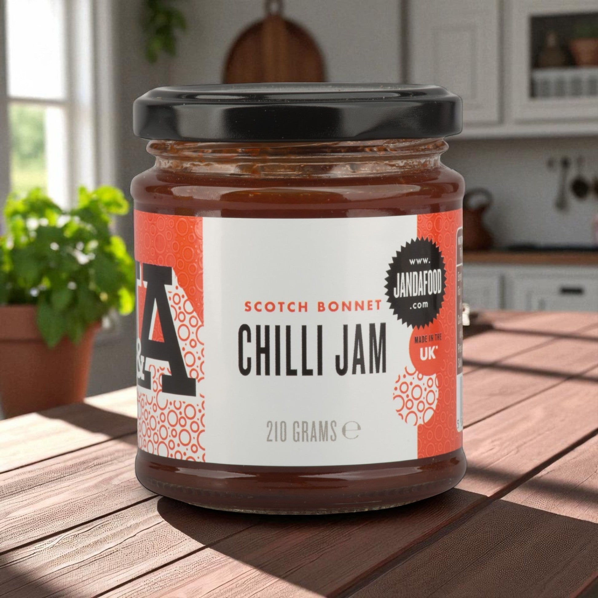 Janda Food Scotch Bonnet Chilli Jam in a 210g glass jar with a black lid, sitting on a wooden table in a kitchen.