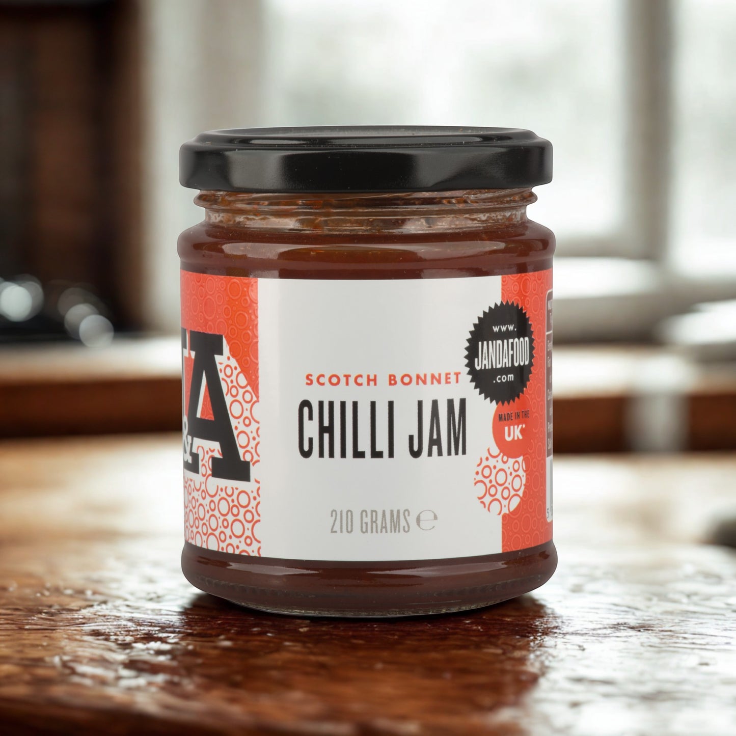 Janda Food Scotch Bonnet Chilli Jam in a 210g glass jar with a red and white label on a wooden kitchen surface.