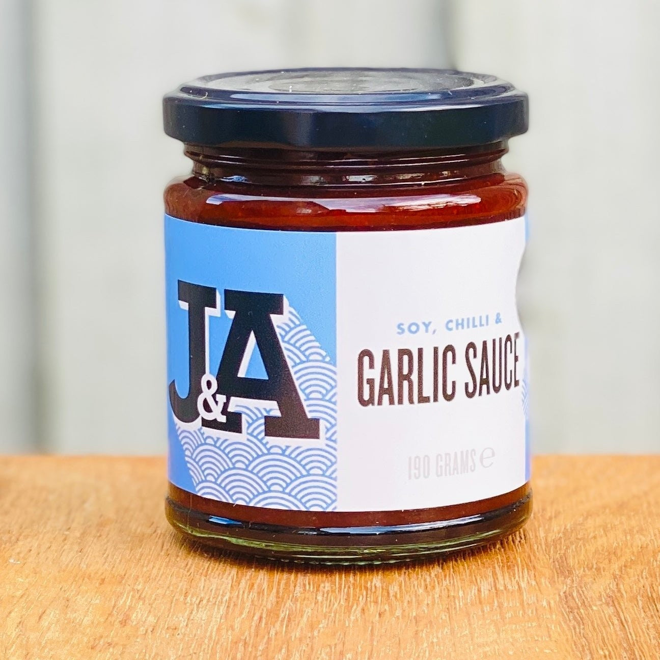 Janda Food Soy, Chilli and Garlic Sauce in a glass jar with a blue and white label on a wooden surface.