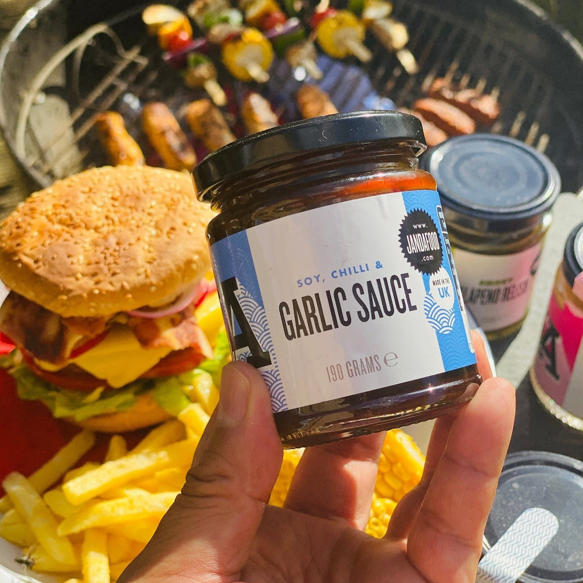 Janda Food handmade soy, chilli and garlic sauce jar held in hand with a grilled burger and fries in the background