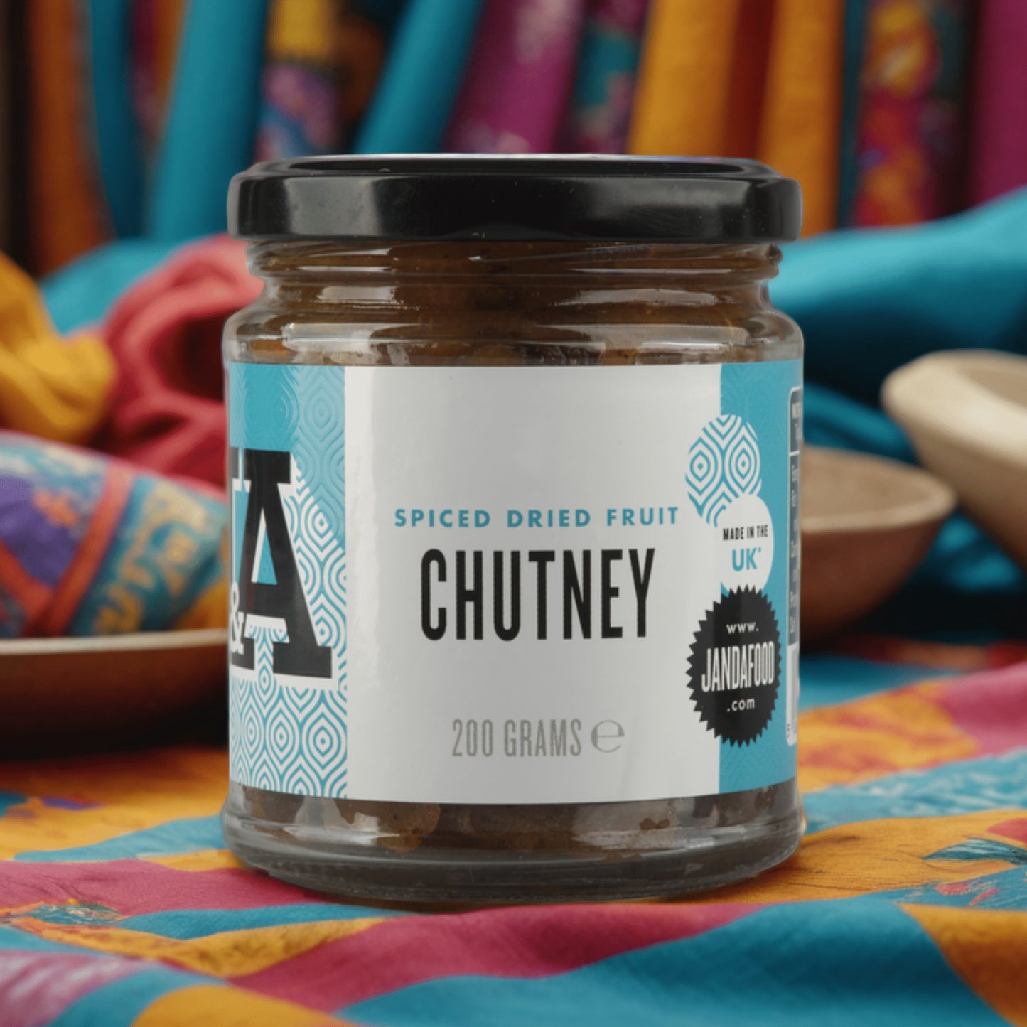 Janda Food Spiced Dried Fruit Chutney in a glass jar with a blue and white label on a colourful patterned cloth