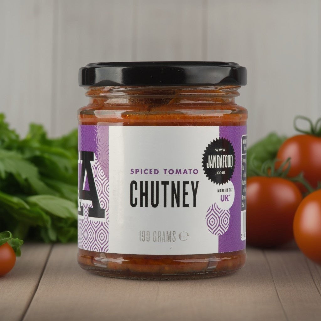 Janda Food spiced tomato chutney in a glass jar with a purple label, surrounded by fresh tomatoes and green herbs.
