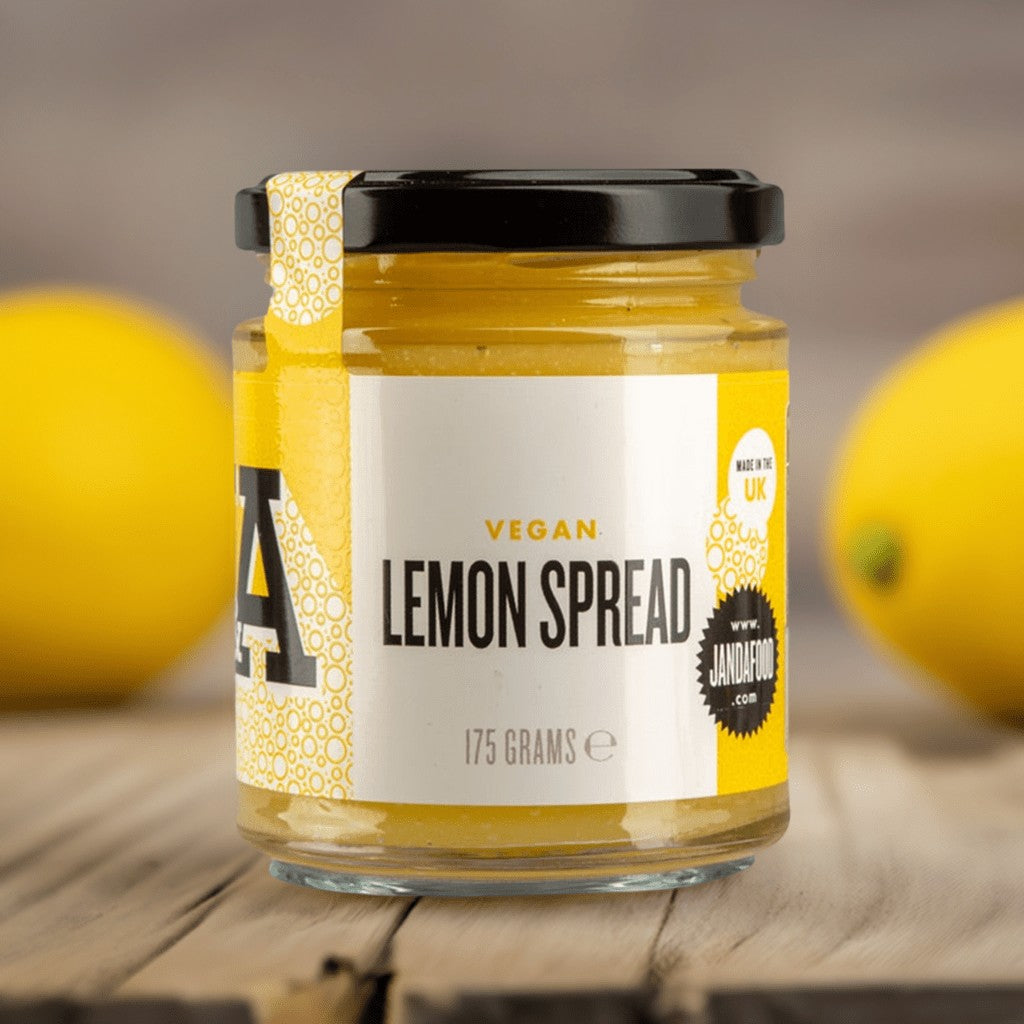 Janda Food vegan lemon spread in a 175g glass jar with a yellow label, set on a wooden surface with fresh lemons.