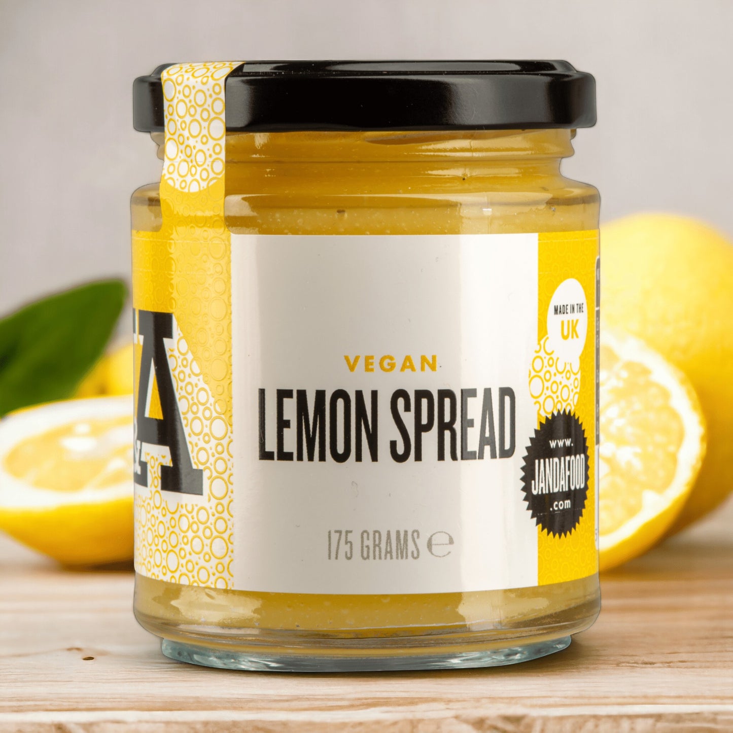 Janda Food vegan lemon spread in a glass jar with a yellow label, set against a background of fresh lemons.