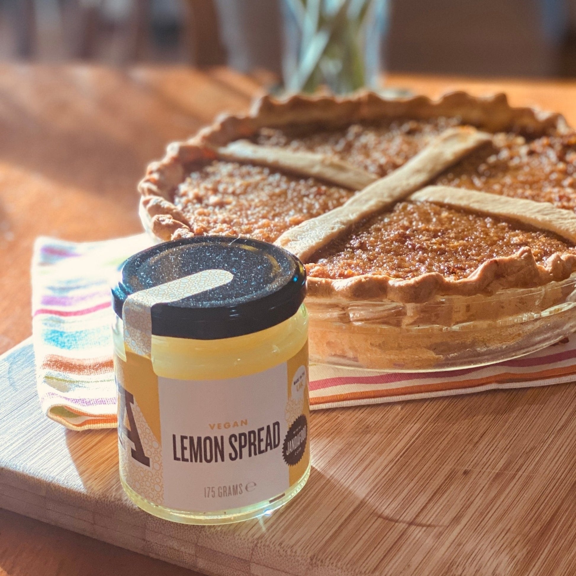 Janda Food vegan lemon spread jar next to a baked tart on a wooden board with a striped napkin