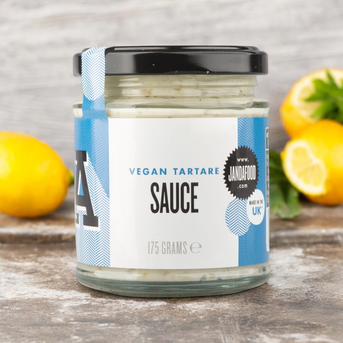 Janda Food vegan tartare sauce in a glass jar with blue and white label, featuring fresh lemons on a wooden surface.