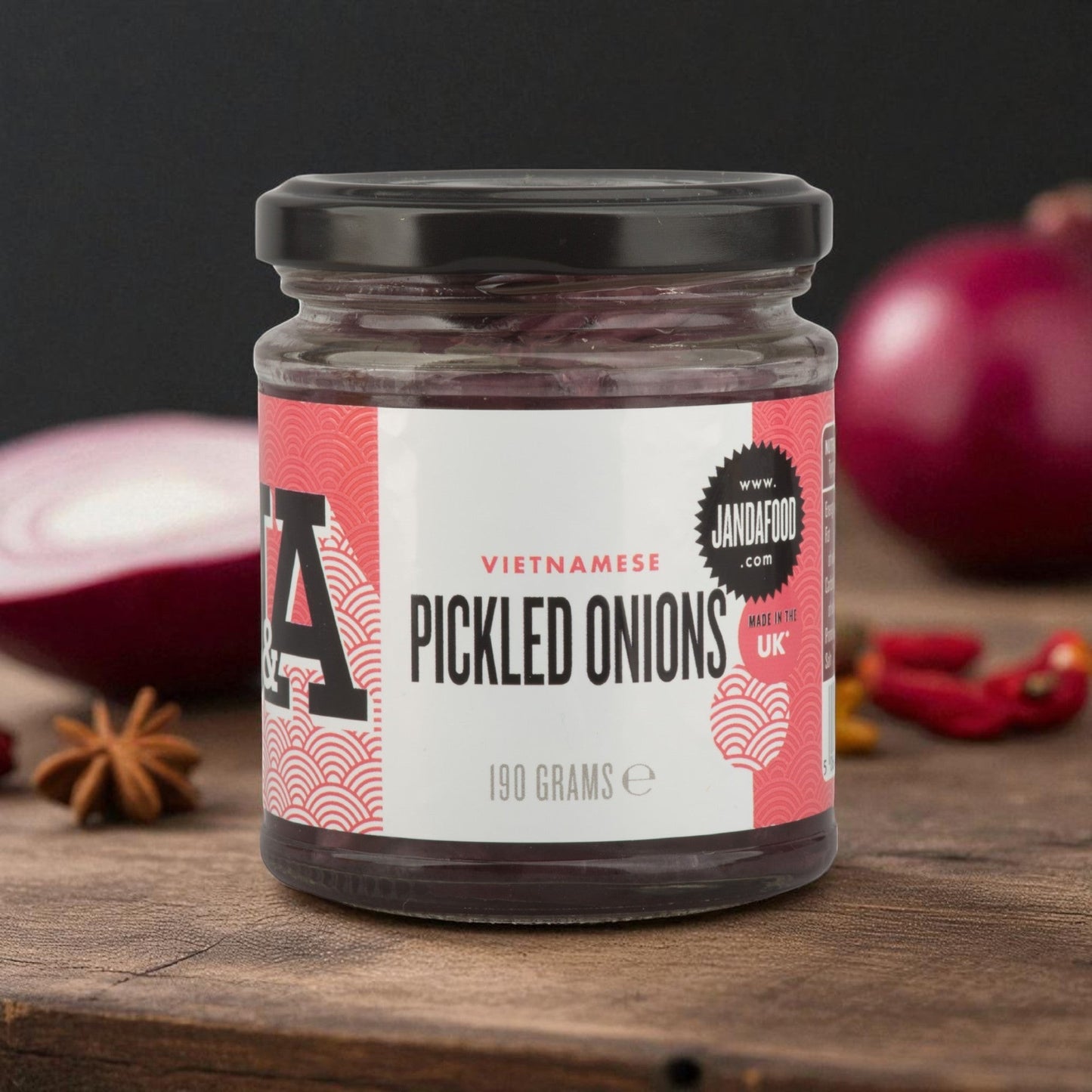 Janda Food Vietnamese pickled red onions in a glass jar on a wooden surface with fresh onion and star anise.